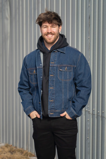 Image of MWG Storm Rider Jean Jacket in navy. MWG Storm Rider jacket has gold stitching and two large chest pockets. Buttons are large and gold in colour. Model is wearing MWG Denim Jacket over a black hoodie and with black MWG stretch denim jeans.