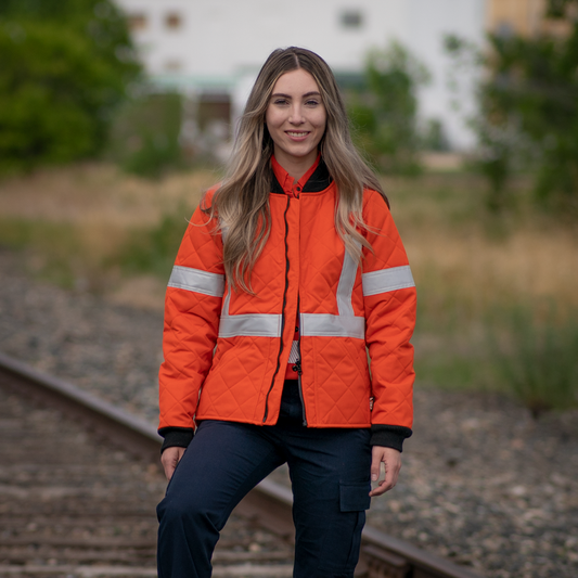 Image of MWG Women's FR freezer jacket. Women's FR Freezer Jacket is bright orange in colour with silver reflective tape on arms and torso to meet high-visibility standard CSA Z96-15. Collar and cuffs are black as well as front zipper. Women's FR Freezer Jacket is made with an inherent flame-resistant (FR) fabric.