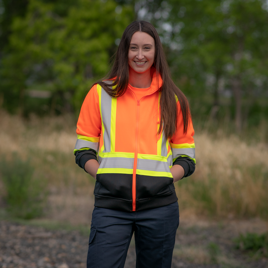 Image of MWG Women's Hi-Vis Hoodie. Women's Hi-Vis Hoodie is bright orange and black in colour with yellow/silver/yellow reflective tape on torso and sleeves to meet high-visibility standard CSA Z96-15. Model is wearing Women's Hoodie with MWG COMFORT WEAVE Women's FR Utility Pant.