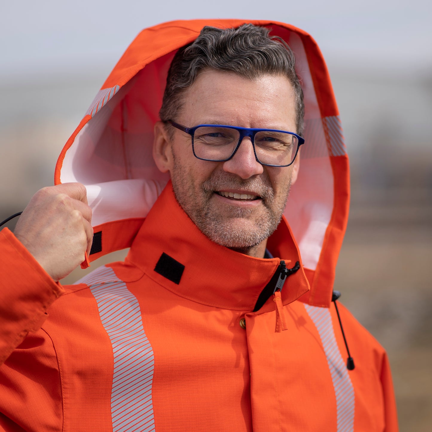 Close up image of the detachable hood on the MWG STORMSHIELD FR Rain Jacket. Detachable hood uses velcro for a quick and secure attachment. Hood has a bright orange exterior and white inner lining. Outside of hood has silver segmented reflective tape from ear-to-ear to meet high-visibility standard CSA Z96-15. MWG STORMSHIELD is a laminated inherent flame-resistant (FR) fabric.