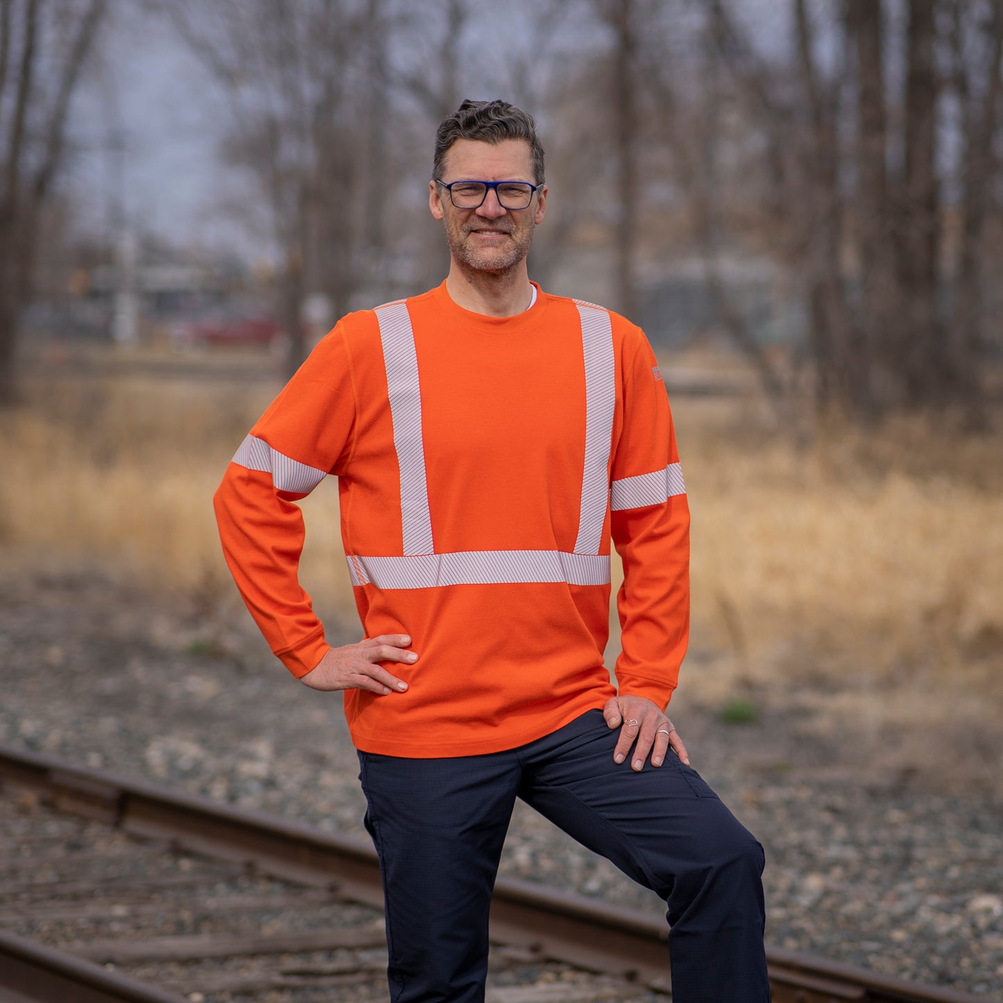 Image of MWG EVOLUTION FRC long-sleeve t-shirt. MWG EVOLUTION FR Shirt is bright orange in colour with silver segmented reflective tape to meet high-visibility standard CSA Z96-15. MWG EVOLUTION is a lightweight inherent flame-resistant (FR) fabric. Model is wearing a size Large MWG FR shirt with navy MWG RIPGUARD FR pants.