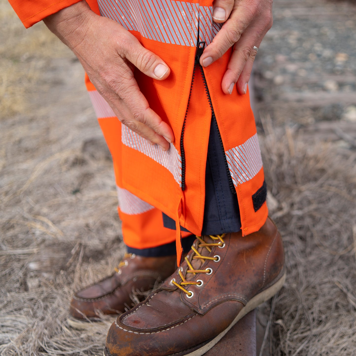 Close up image of 18" leg zippers and velcro closure on MWG STORMSHIELD FR Rain Proof Bib. Image displays silver segmented reflective tape on lower legs to meet high-visibility standard CSA Z96-15. Leg zipper and velcro are both black in colour.