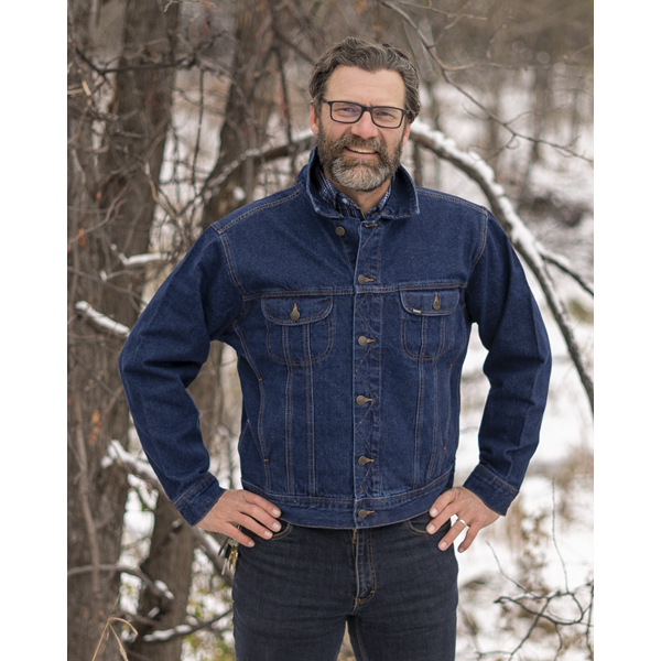 Image of MWG Storm Rider Men's Denim Jacket. MWG Men's Jean Jacket is navy in colour with gold stitching and gold buttons. Denim jacket has two large chest pockets and two side slant pockets on hips. Model is wearing Storm Rider Jacket with the collar up and MWG stretch denim blue jeans for bottoms.