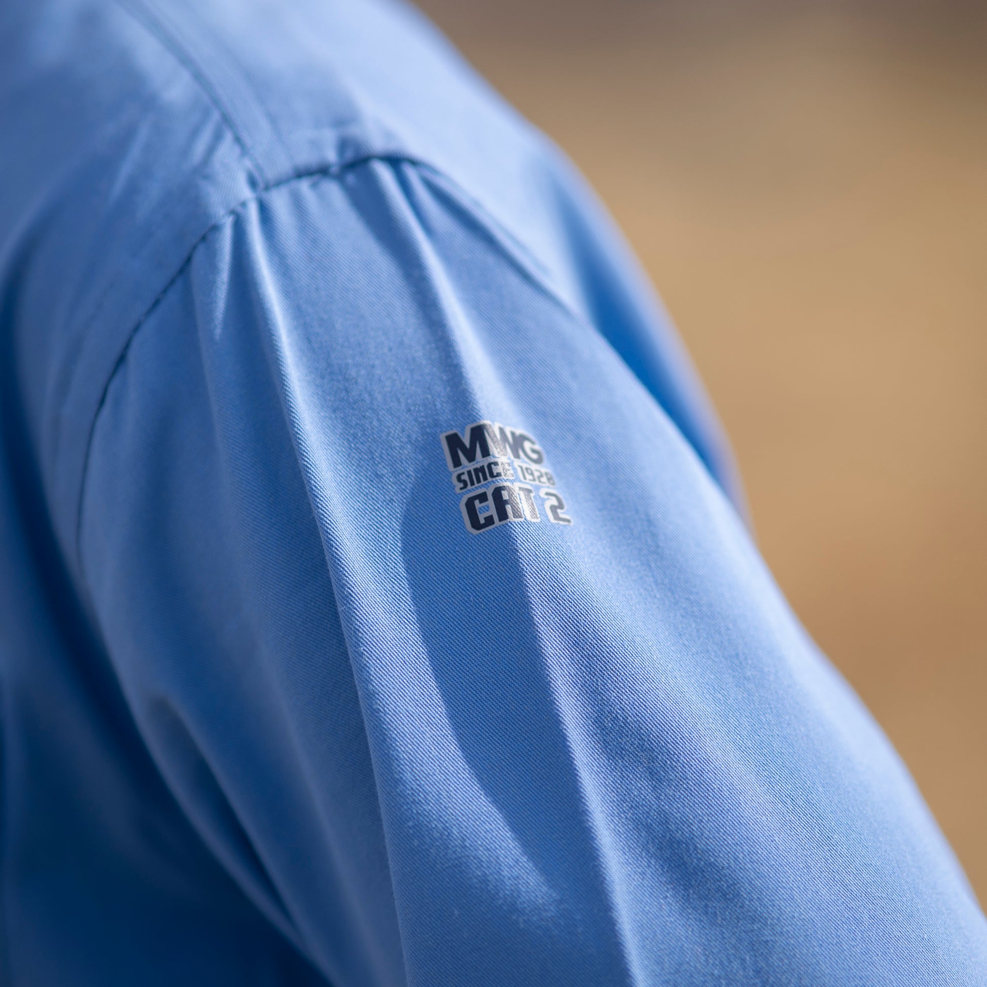Close up image of MWG COMFORT WEAVE FR Uniform Shirt in light blue. Image displays MWG logo on sleeve with CAT 2 identification, symbolizing level of flame-resistance.