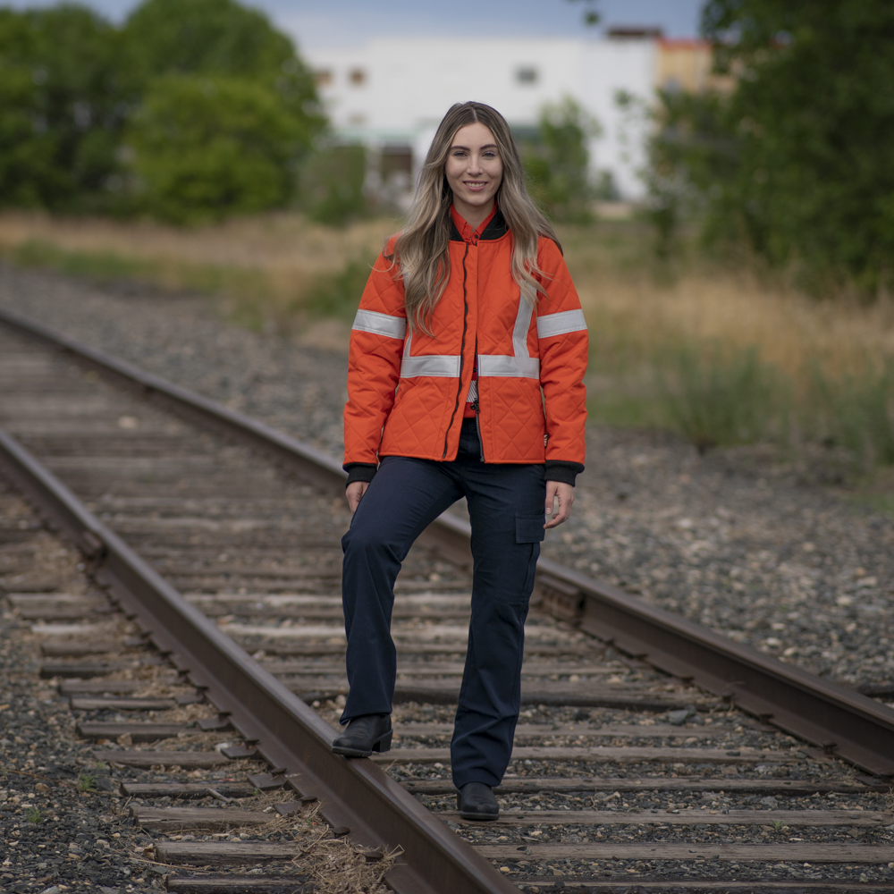 Image of MWG Women's FR freezer jacket. Women's FR Freezer Jacket is bright orange in colour with silver reflective tape on arms and torso to meet high-visibility standard CSA Z96-15. Collar and cuffs on freezer jacket are black as well as front zipper. MWG Women's FR Freezer Jacket is made with an inherent flame-resistant (FR) fabric.