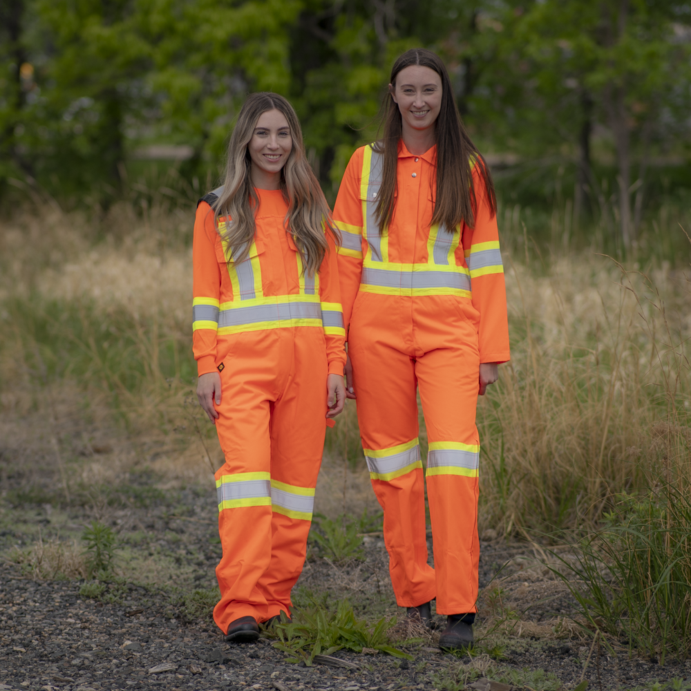 Image of MWG Women's Hi-vis Bib Overall. Women's Overall is bright orange in colour with yellow/silver/yellow reflective tape on torso and legs to meet high-visibility standard CSA Z96-15. MWG Hi-Vis Overall is a women's fit.
