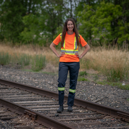 Image of MWG Women's Hi-Vis cargo pant. Women's Cargo Pant is navy in color with yellow/silver/yellow reflective tape on lower legs to meet high-visibility standard CSA Z96-15. Model is wearing navy cargo pant with Women's Hi-Vis T-Shirt.