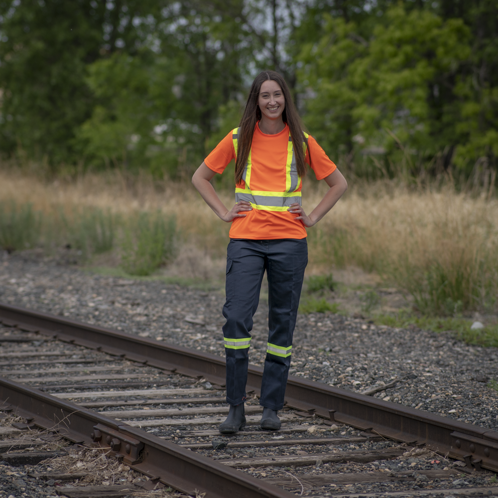 Image of MWG Women's Hi-Vis T-Shirt. Women's Hi-Vis T-Shirt is bright orange in colour with yellow/silver/yellow reflective tape on torso to meet high-visibility standard. Model is wearing Hi-Vis Shirt with navy Hi-Vis cargo pant. Both are a women's fit.