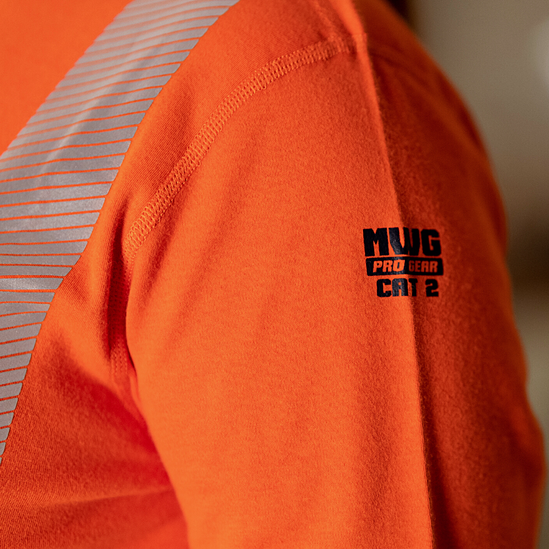 Close up image of MWG Pro Gear logo and CAT 2 label on MWG EVOLUTION Women's FR Shirt. Logo is black on a bright orange background.