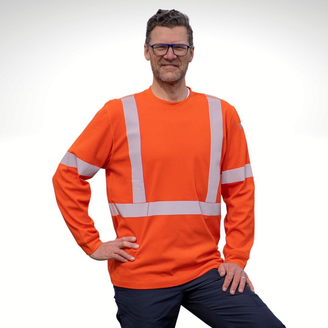 Image of MWG EVOLUTION FRC long-sleeve t-shirt. MWG EVOLUTION FR Shirt is bright orange in colour with silver segmented reflective tape to meet high-visibility standard CSA Z96-15. MWG EVOLUTION is a lightweight inherent flame-resistant (FR) fabric. Model is wearing a size Large MWG FR shirt with navy MWG RIPGUARD FR pants.