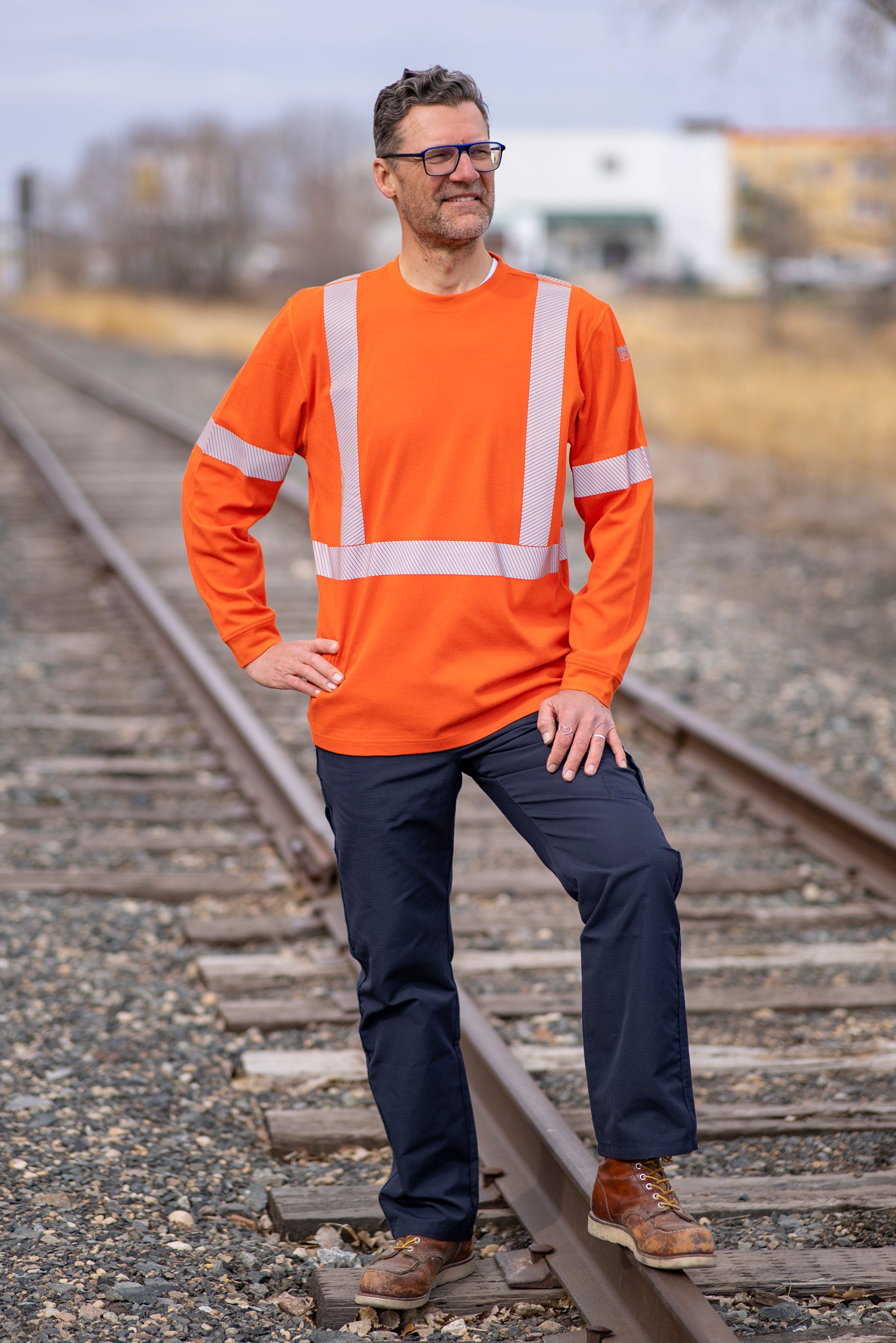 Image of MWG EVOLUTION FRC Long-Sleeve T-Shirt. MWG EVOLUTION FR Shirt is bright orange in colour with silver segmented reflective tape to meet CSA Z96-15. MWG EVOLUTION is a lightweight inherent flame-resistant (FR) fabric. Model is wearing a size Large MWG EVOLUTION FR Shirt with MWG RIPGUARD FR utility pants.