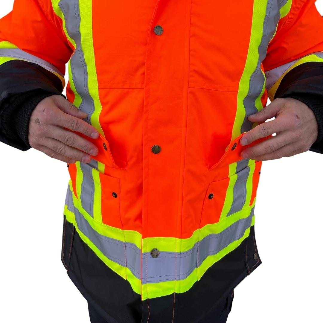 Close up of pocket flaps on men's hi-vis winter jacket. Hi-Vis Winter Jacket has two large pockets with flaps. Hi-Vis Jacket is bright orange and black with yellow/silver/yellow striping for hi-vis compliance.