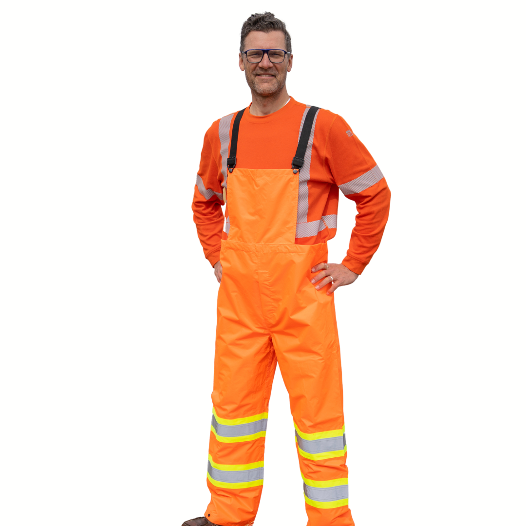 Image of MWG Hi-Vis bib rain pant. Hi-Vis bib rain pant is bright orange in colour with yellow/silver/yellow reflective tape on lower leg to meet high-visibility standard CSA Z96-15. Model is wearing Hi-Vis bib rain pant over orange MWG EVOLUTION long-sleeve t-shirt.