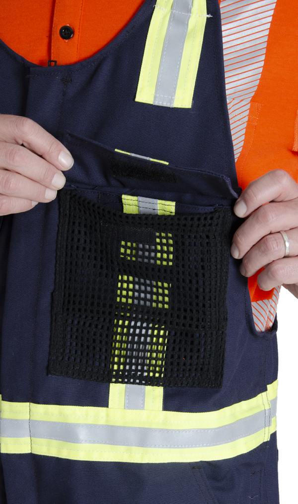 Close up view of mesh chest pocket on MWG Duck Canvas flame-resistant (FR) bib overall. Mesh is black in colour with navy flap hanging over top. Yellow/silver/yellow reflective is seen underneath the mesh pocket.