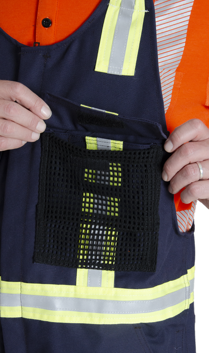 Close up view of mesh chest pocket on MWG Duck Canvas flame-resistant (FR) bib overall. Mesh is black in colour with navy flap hanging over top. Yellow/silver/yellow reflective is seen underneath the mesh pocket.