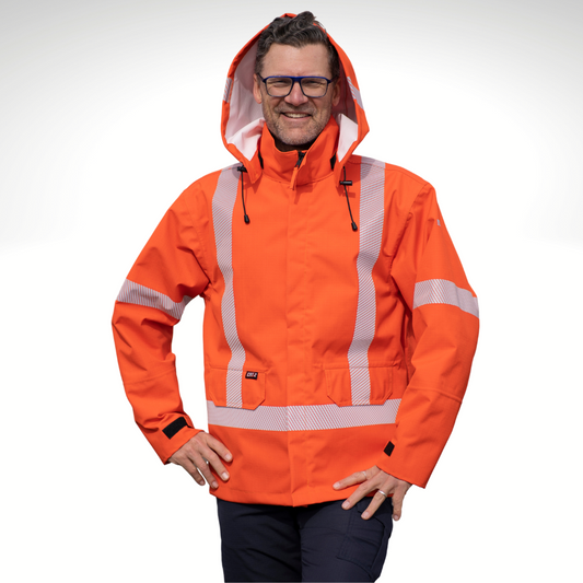 Image of MWG STORMSHIELD FR Rain Jacket. FR Rain Jacket is bright orange with silver segmented reflective tape on torso and sleeves to meet CSA Z96-15 high-visibility standard. MWG STORMSHIELD is an inherent flame-resistant (FR) fabric that's been laminated for wind and waterproofness. Model is wearing FR Rain Jacket with navy MWG RIPGUARD FR Pants.