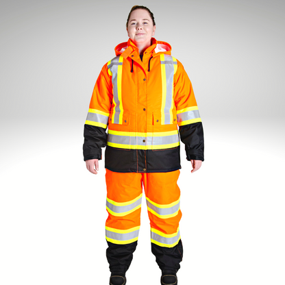 Image of MWG Women's Hi-Vis Insulated Parka Jacket. Women's Hi-Vis Parka is bright orange and black. Yellow/silver/yellow reflective striping on torso, waist, and sleeves to meet high-visibility standard CSA Z96-15. Model is wearing Women's Hi-Vis Parka with hi-viz insulated bib overalls.