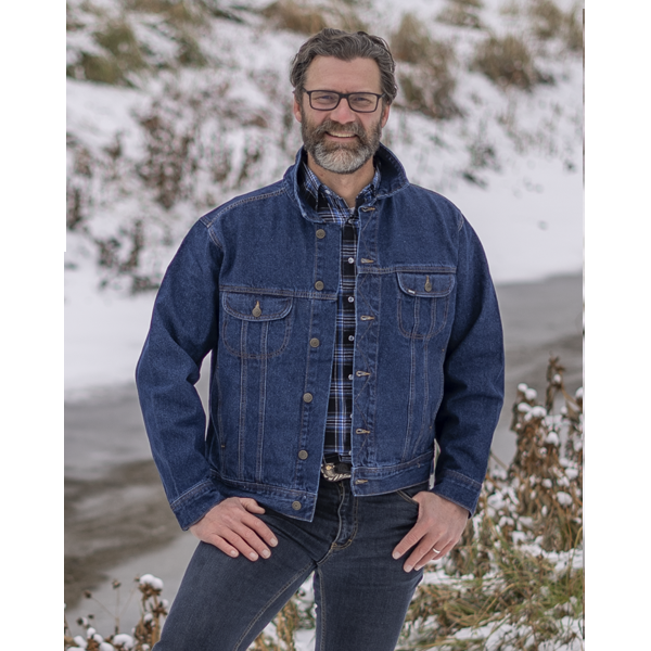 Image of MWG Storm Rider jean jacket. Storm Rider jacket is navy in colour with gold stitching and buttons. Jacket has two large chest pockets. Model is wearing MWG Storm Rider Jacket with collar up, over a blue and black MWG snap flannel shirt.