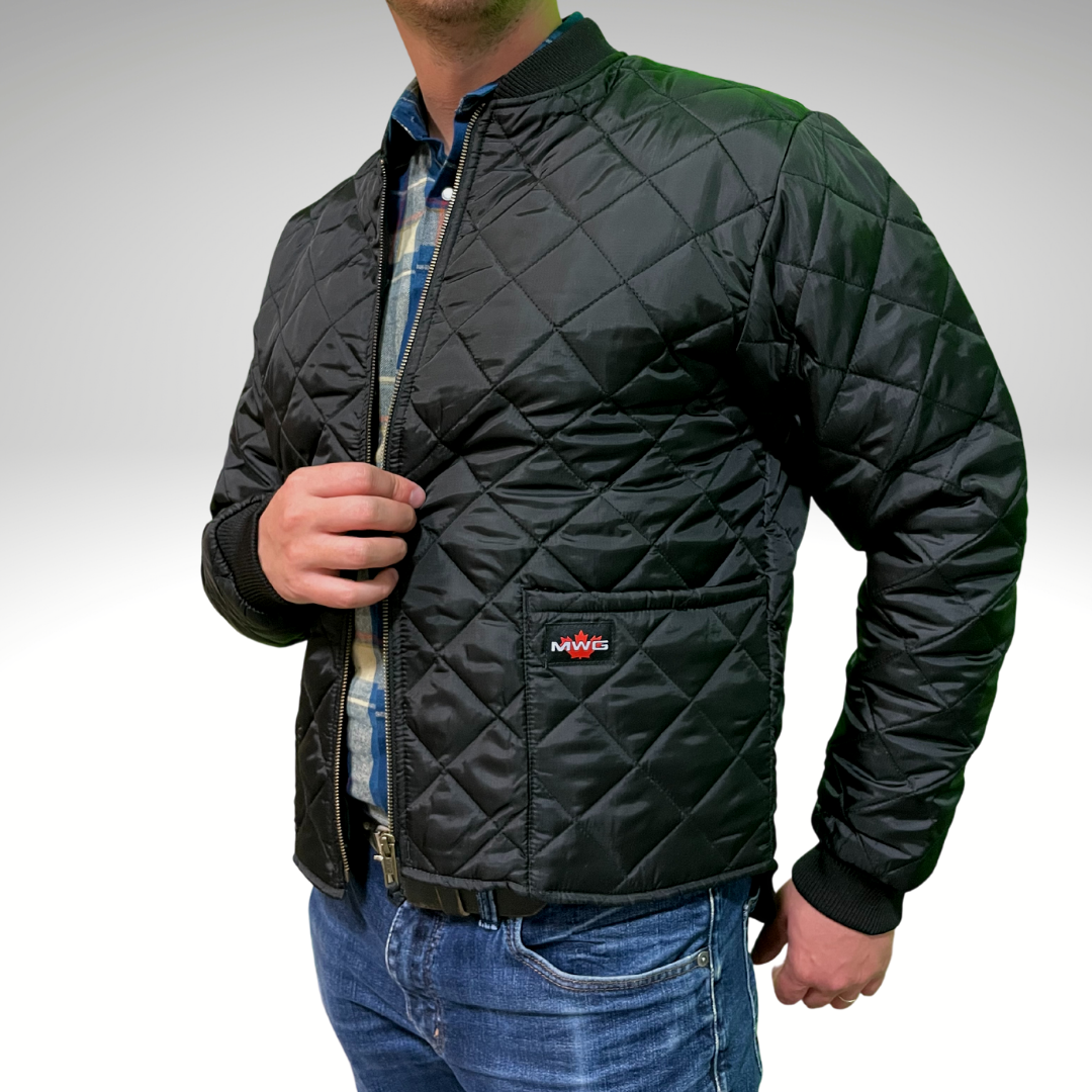 Image of MWG Men's Ripstop Freezer Jacket. Men's Ripstop Freezer Jacket is all black with a knit ribbed collar and cuffs. Freezer Jacket is made with a 3" diamond quilt and a ripstop fabric for durability. Image shows brass zipper and MWG maple leaf logo.