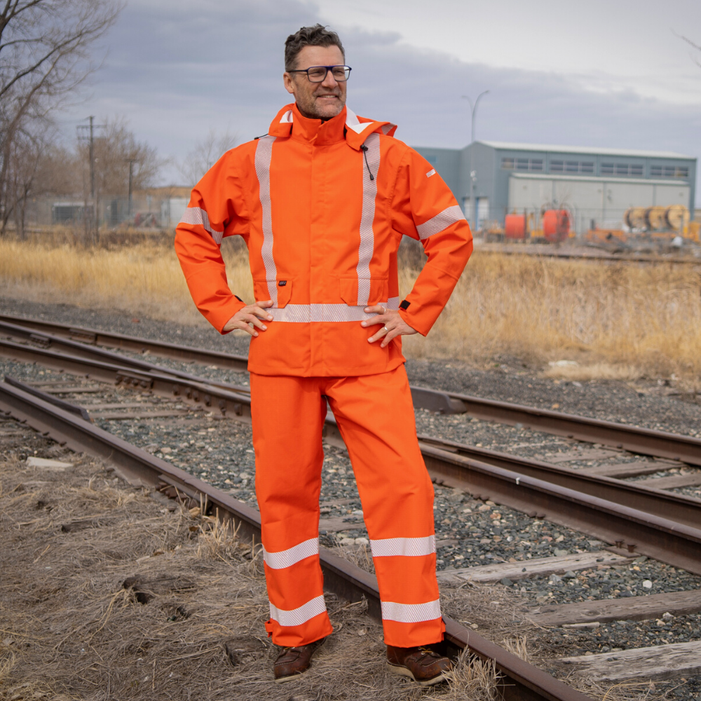 Image of MWG STORMSHIELD FR Rain Proof Bib. MWG STORMSHIELD FR Bib is bright orange in colour with silver segmented reflective tape on lower legs to meet high-visibility standard CSA Z96-15. Model is wearing MWG STORMSHIELD FR Bib with bright orange MWG STORMSHIELD FR rain jacket. MWG STORMSHIELD is a laminated inherent flame-resistant (FR) fabric.